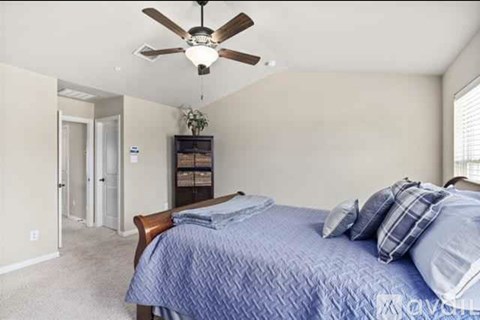 A bedroom with a bed, pillows, a ceiling fan, and a nightstand with a lamp.
