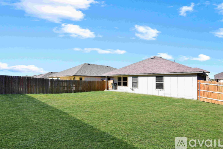A house with a brown roof and a white exterior is surrounded by a wooden fence and a green lawn.