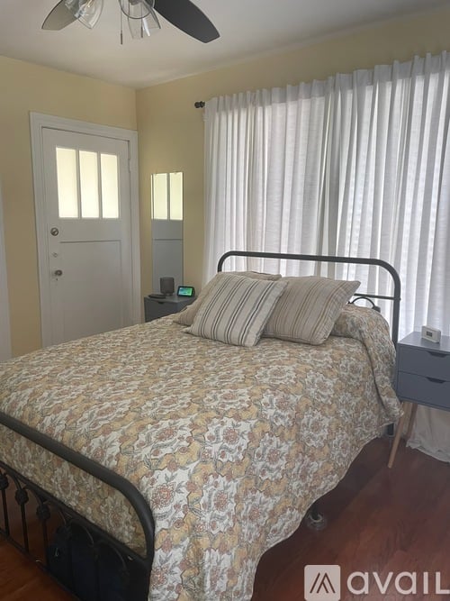 A bedroom with a bed, nightstand, and window with curtains.