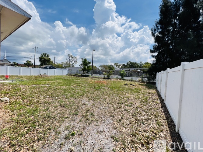 A large, open, grassy field with a white fence on one side and a building on the other.