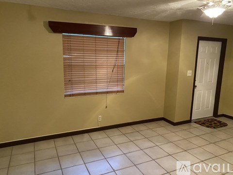 A room with a window covered in blinds, a door, and a light switch on the wall.