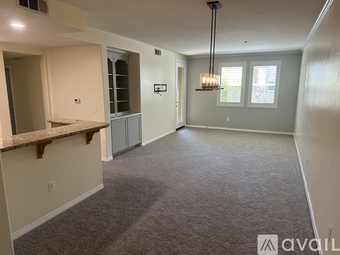 A spacious room with a carpeted floor, a window with white blinds, and a hanging light fixture.
