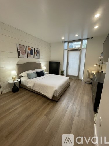 A bedroom with a large bed, a nightstand with a lamp, and a wall-mounted TV.