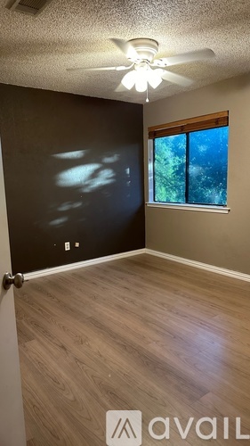 A room with a ceiling fan and a window showing trees outside.