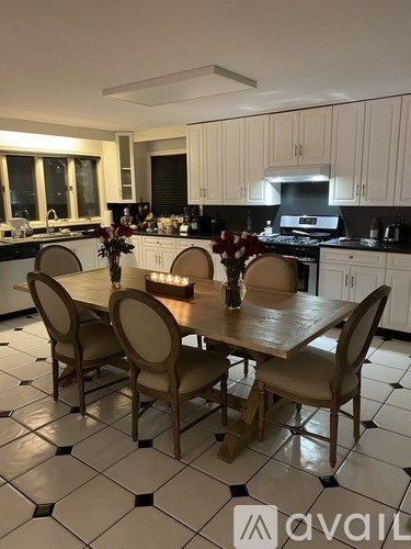 A kitchen with a table set for six with a vase of flowers in the middle.