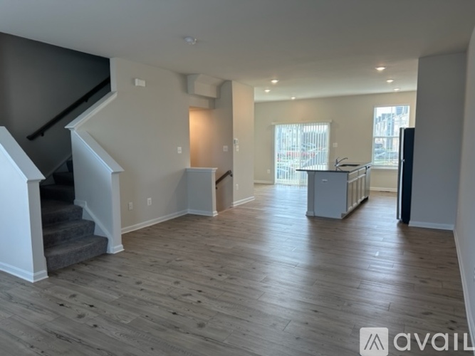 A spacious living room with wooden flooring and a staircase on the left side.