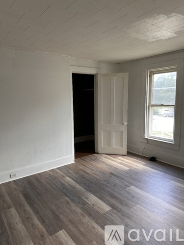 A room with wooden flooring and a window with a view of a parking lot.