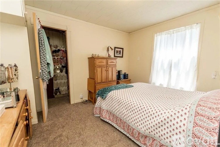 A bedroom with a bed, dresser, and a closet with clothes hanging.