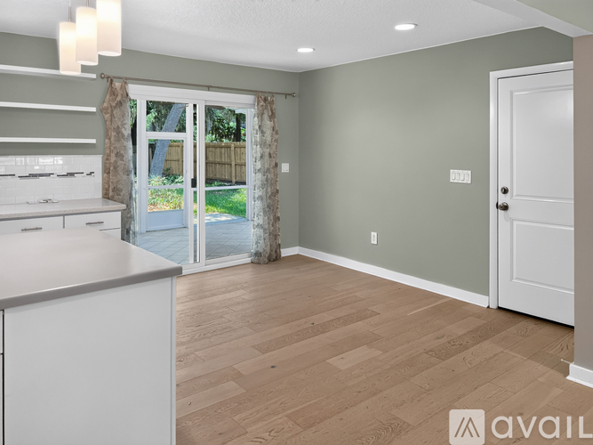 A kitchen with a white counter and cabinets with a sliding glass door leading outside.