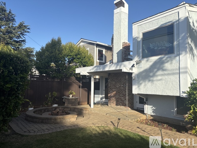 A house with a white exterior and a brick chimney is surrounded by a fence and has a small garden area.