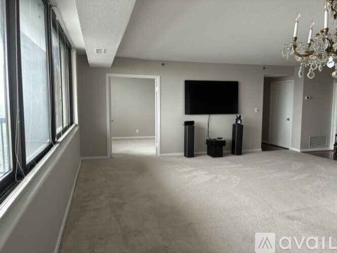 A spacious living room with a chandelier and a flat-screen TV mounted on the wall.