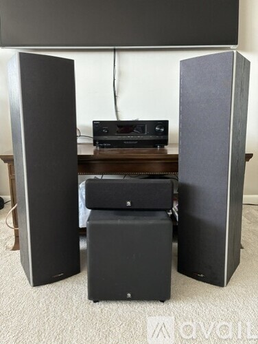 A pair of black speakers stand upright on a carpeted floor.