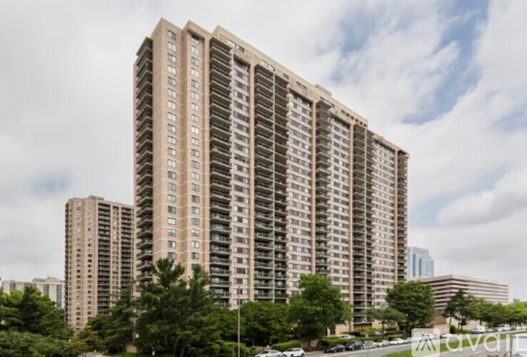 A tall residential building with many windows is surrounded by other buildings and trees.