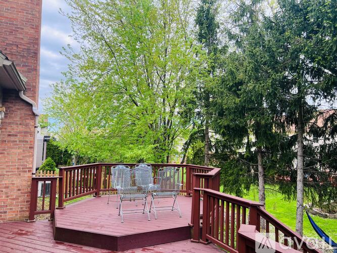 A wooden deck with a glass table and chairs surrounded by trees.