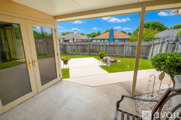 A patio with a glass door opens to a backyard with a fence and a house in the background.