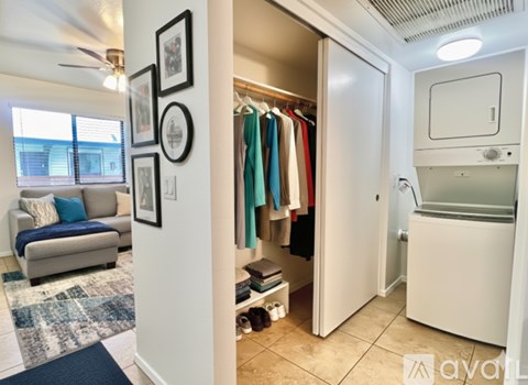 A room with a couch, a fan, and a wall with pictures and a closet with clothes.