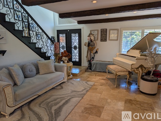 A living room with a grand piano and a staircase with a black railing.