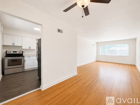 A room with a ceiling fan and a kitchen area with stainless steel appliances.