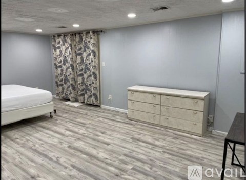 A bedroom with a bed, dresser, and a wooden floor.