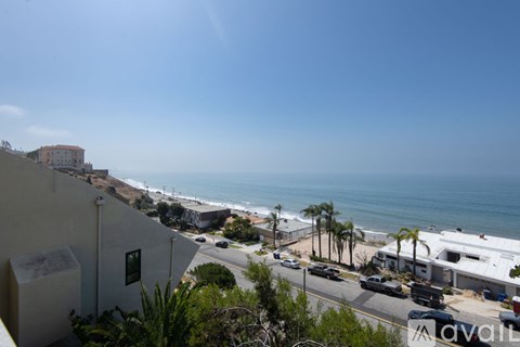 A view of a coastal area with a clear blue sky and a few buildings and cars visible.