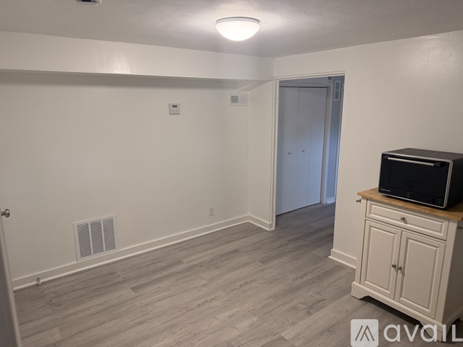 A room with a wooden floor, a white door, and a white wall with a small window.