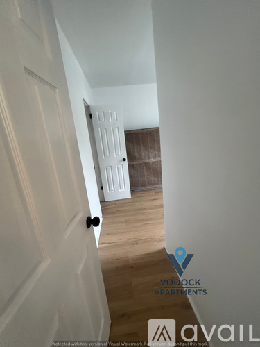 A hallway with a door on the left and a bedroom on the right.