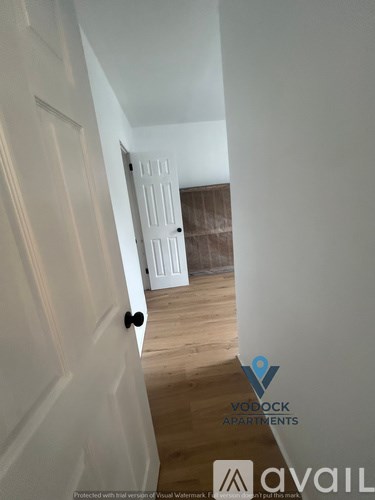 A hallway with a door on the left and a bedroom on the right.