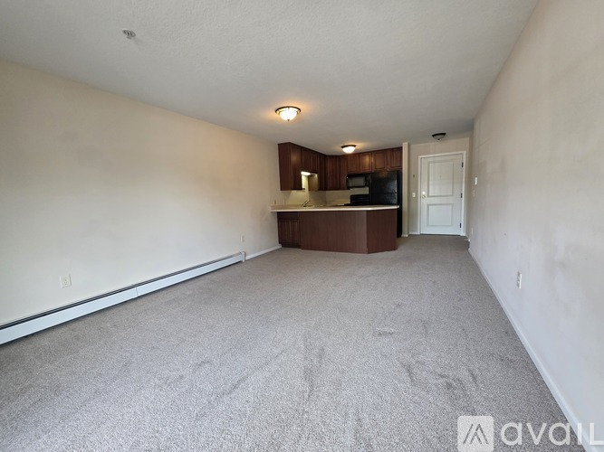 A room with a carpeted floor and a small kitchenette in the corner.