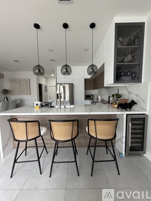 A kitchen with a white countertop and three chairs with woven seats.