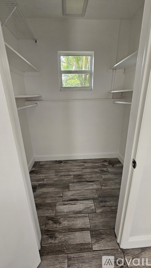A small white closet with a window and wood flooring.