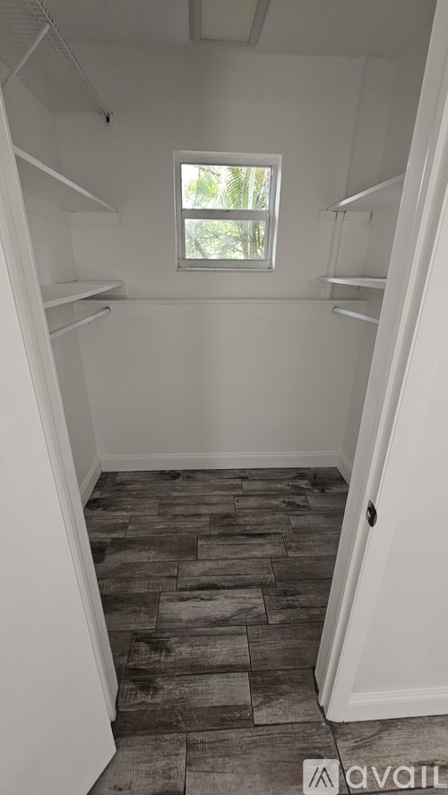 A small, empty room with a window and wooden flooring.