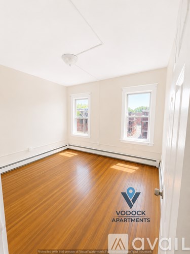 A room with wooden floors and two windows, one of which has a view of a building.