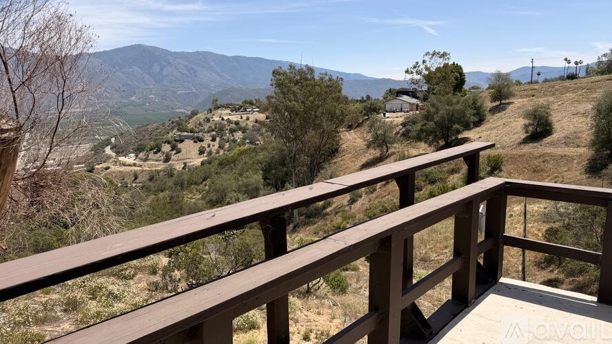 A wooden balcony overlooks a valley with trees and mountains in the distance.