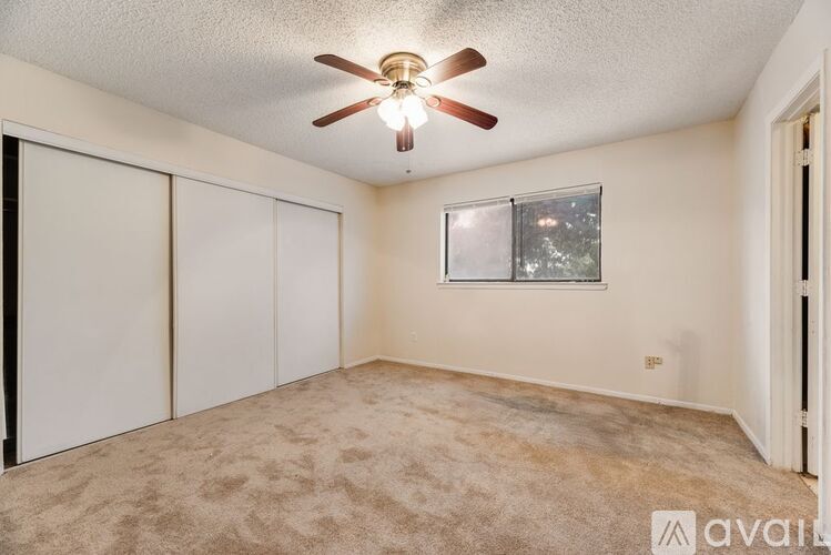 A room with a ceiling fan and a window with a view of trees outside.