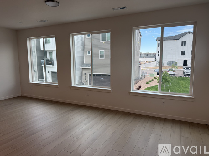 A spacious room with three windows overlooking a residential area.