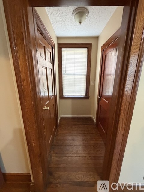 A hallway with wood floors and a window with blinds.