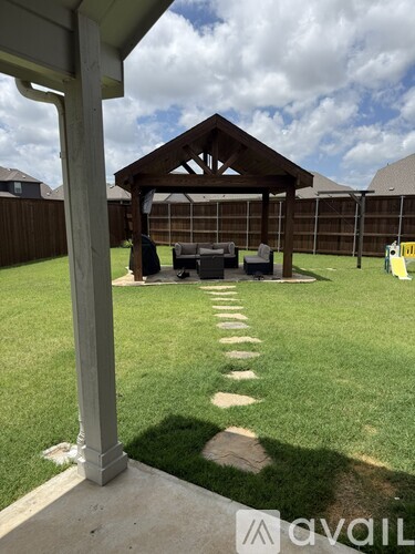 A wooden gazebo is situated in a backyard with a lawn and a stone pathway leading to it.