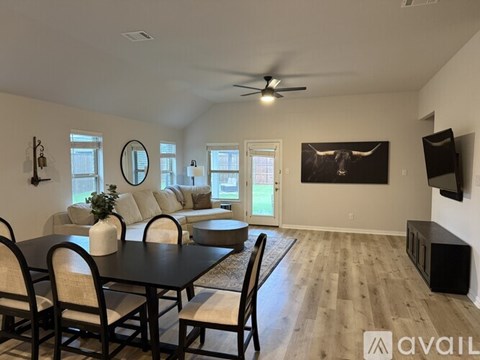 A living room with a black table and chairs, a television, and a large window.