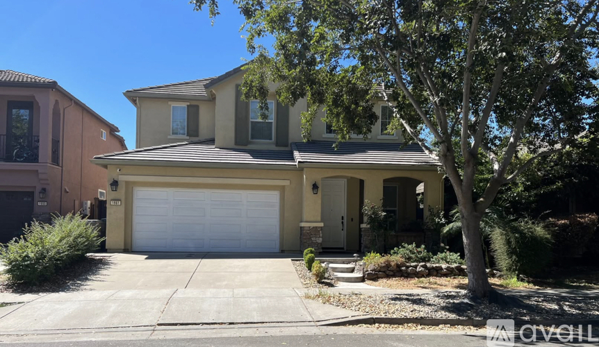 A house with a garage door and a tree in front.
