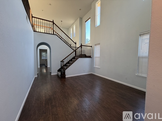 A spacious room with a wooden floor and a staircase with a black railing.