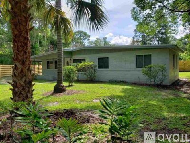 A house with a white exterior is surrounded by greenery and palm trees.