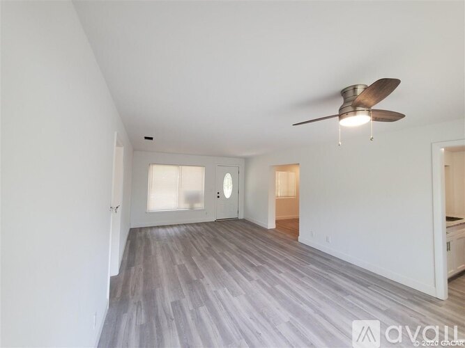 A spacious room with a ceiling fan and light, and a wooden floor.