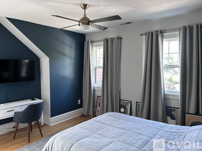 A bedroom with a bed, desk, and window with curtains.