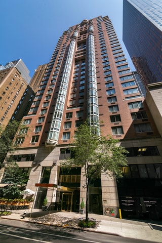 A tall building with a glass facade stands in front of a tree.