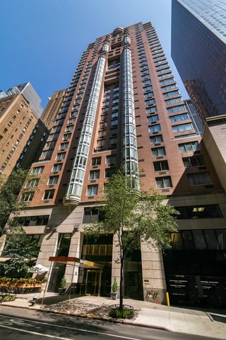 A tall building with a glass facade stands in front of a tree.