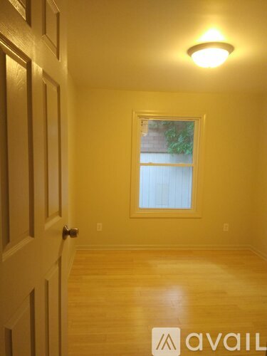 A room with a wooden floor and a window with a white curtain.