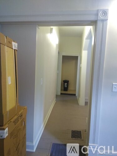A hallway with a door on the left and a trash can in the distance.