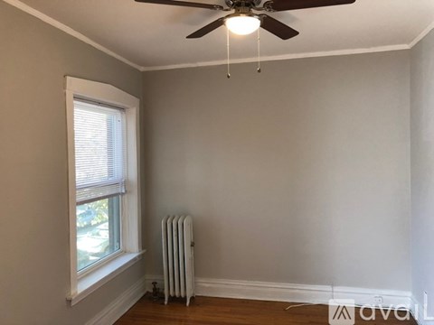 A room with a ceiling fan, a window with blinds, and a white radiator on the floor.