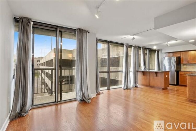 A spacious room with wooden floors and large windows with curtains.