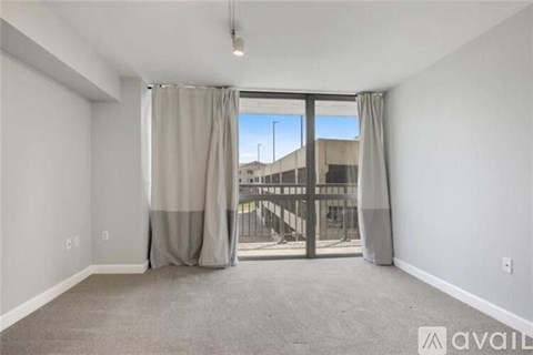 A room with a carpeted floor, a sliding glass door with curtains, and a view of a building outside.